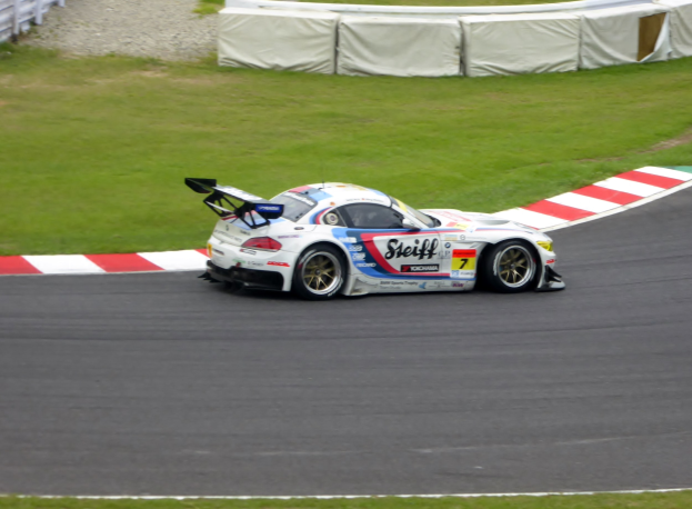 Ein Porsche 911 GT3 RSR Rennauto auf einer Rennstrecke, umgeben von grünem Gras und einem Zaun auf der linken Seite, verziert mit Text und Zahlen für die 24 Stunden von Le Mans.