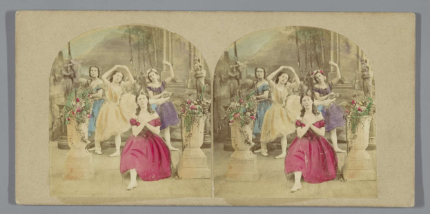 Ein Schwarz-Weiß-Foto von Frauen in bunten Kleidern, die auf einer dekorierten Bühne mit Blumenvasen und grünen Bäumen im Hintergrund tanzen.