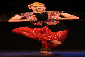 Ein Mann in roter und schwarzer Kleidung tanzt auf der Bühne mit geschlossenen Augen und leicht geöffnetem Mund.