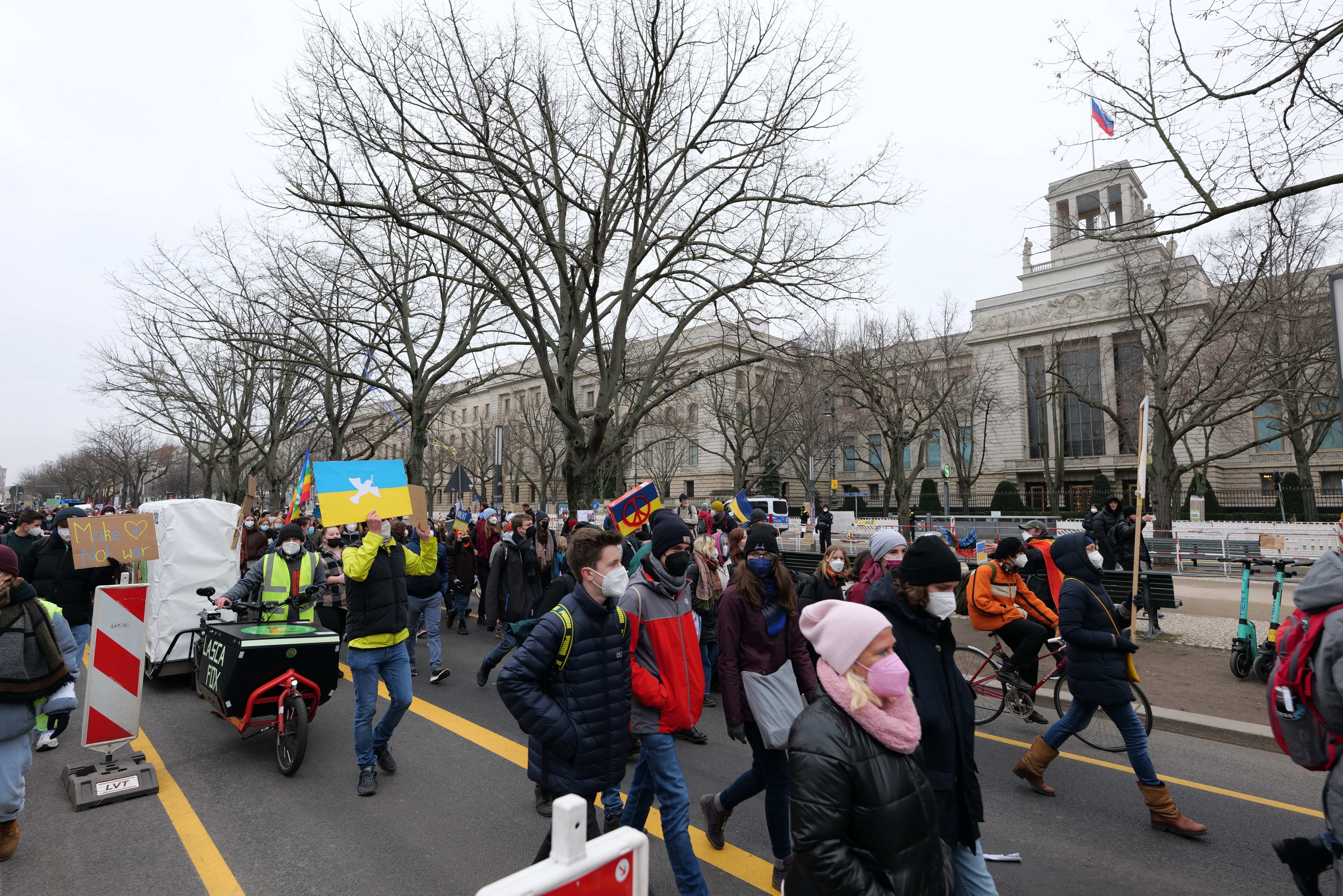 Eine große Protestdemonstration mit Menschen, die eine Straße in Washington, D.C. entlanggehen, einige halten Schilder und andere fahren Fahrräder, mit Bäumen und einem klaren blauen Himmel im Hintergrund.