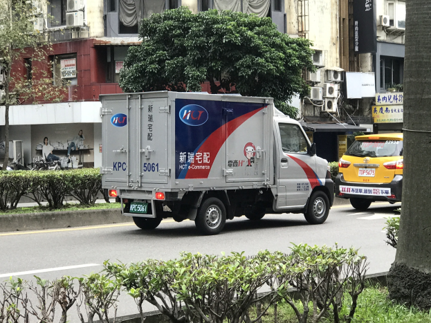 Ambulanz auf dem Seitenstreifen neben einem Baum geparkt, mit Fahrzeugen, Gebäuden und anderen Objekten im Hintergrund.