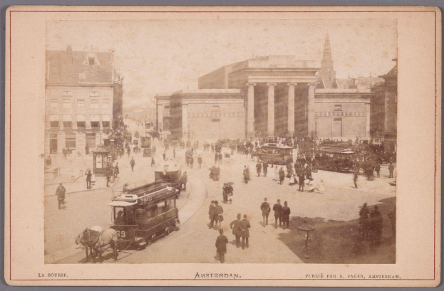 Ein altes Foto einer belebten Straßenkreuzung in Amsterdam mit Menschen, Fahrzeugen, Laternenmasten und Gebäuden, mit Text am unteren Bildrand.