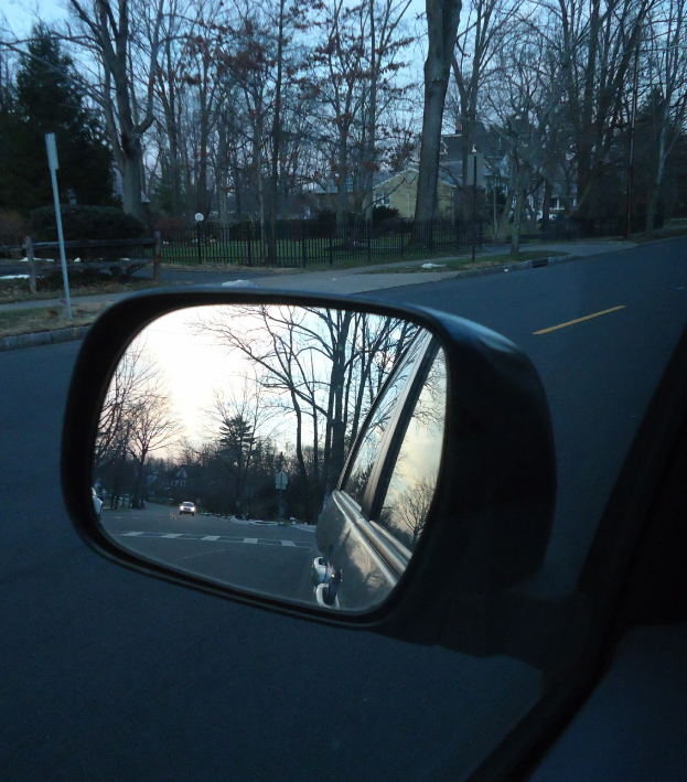 Seitenspiegel eines Autos reflektiert Bäume, Gebäude und Himmel