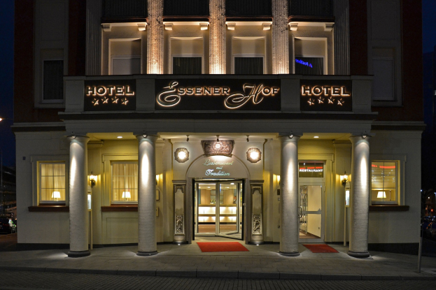 Das Essenerhof Hotel in Berlin, Deutschland, ein mehrstöckiges Gebäude mit Fenstern, Türen, Säulen und einem Namensschild, mit einer Straße und Fahrzeugen davor und einem sichtbaren Himmel im Hintergrund.
