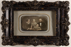 Altes Familienfoto in einem prunkvoll verzierten Rahmen auf einer weißen Oberfläche, mit der Familie, die in die Kamera lächelt.