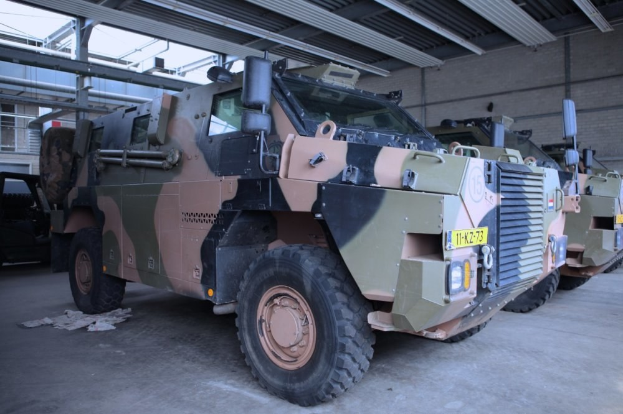Eine Gruppe von Militärfahrzeugen mit Rädern, die in einem Gebäude geparkt sind, neben einer Wand auf der rechten Seite und einem Schuppen oben.