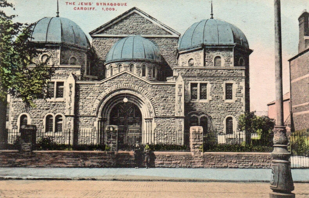 Schwarz-weiß-Postkarte der jüdischen Synagoge in Cardiff, Ontario, Kanada, zeigend ein Gebäude mit Fenstern, Türen und Bögen, umgeben von Pflanzen, einem Zaun, Bäumen, einem Pfahl und einem bewölkten Himmel, mit Text oben.