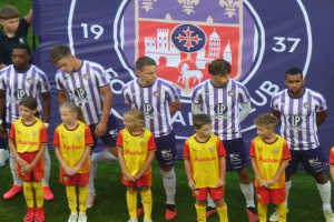 Gruppe junger Menschen auf einem Fussballfeld mit einem Banner im Hintergrund, auf dem "Preston Primary School Football Team" steht.