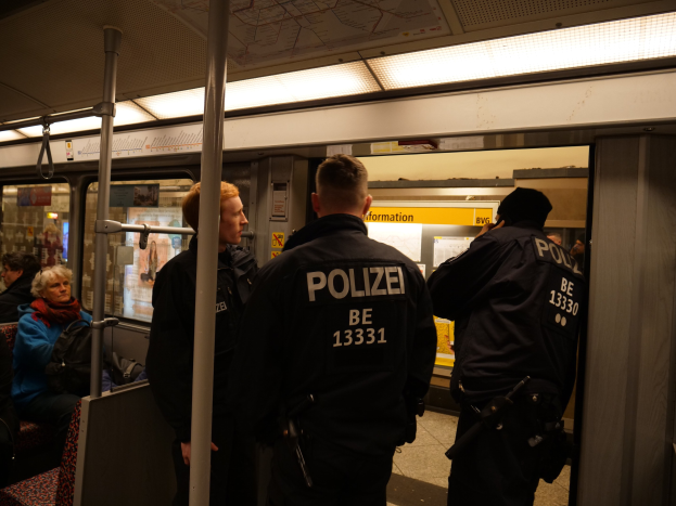 Eine Gruppe von Polizisten steht zusammen auf einer U-Bahn, während andere Fahrgäste sitzen oder stehen, beleuchtet von Deckenlampen.