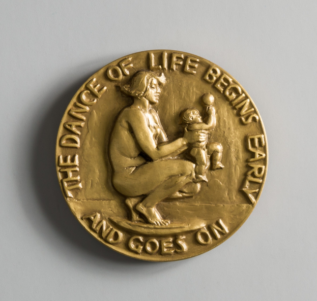 Goldmedaille mit der Inschrift "Der Tanz des Lebens beginnt früh und geht weiter", dargestellt von einer Frau mit einem Baby.