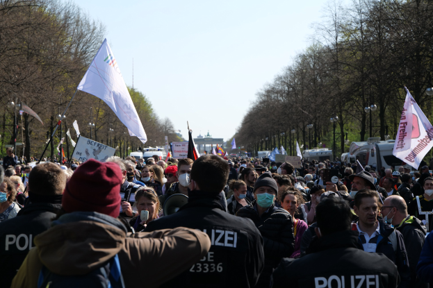 Eine große Gruppe von Menschen vor einer Reihe von Polizeibeamten, einige mit Mützen und Masken, bei einer Demonstration in Berlin, Deutschland.