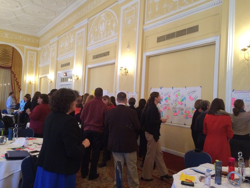 Menschen betrachten verschiedene Plakate und Diagramme an einer Wand in einem Kunstmuseum.