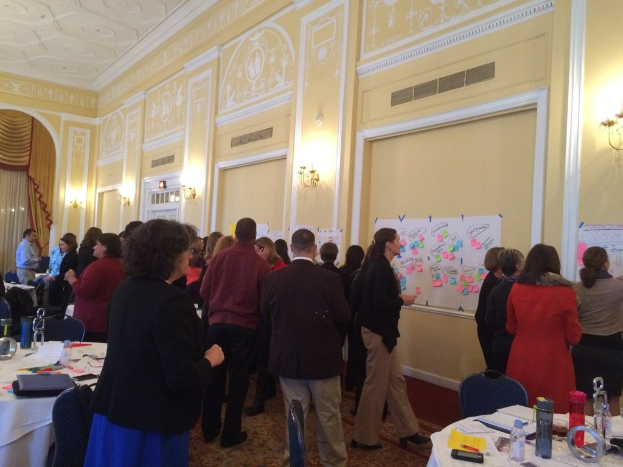 Menschen betrachten verschiedene Plakate und Diagramme an einer Wand in einem Kunstmuseum.