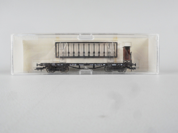 Ein Modell-Gepäckwagen-Auto mit einem schwarz-weißen Karomuster und einem roten Streifen, das in einer durchsichtigen Plastikbox auf einer weißen Oberfläche ausgestellt ist.