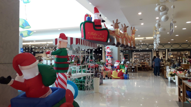 Ein Geschäft voller Weihnachtsdekorationen, darunter Santa Claus- und Rentierfiguren, Spielzeug und Blumenbouquets auf Tischen, mit Menschen auf dem Boden und der Decke mit Lichtern und Ballons geschmückt.