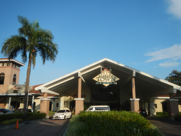 Einfahrt zu einer Resort mit Palmen vorne, umgeben von Gebäuden, Fahrzeugen auf der Straße, Verkehrskegeln, Büschen, Bäumen und einem bewölkten Himmel im Hintergrund.