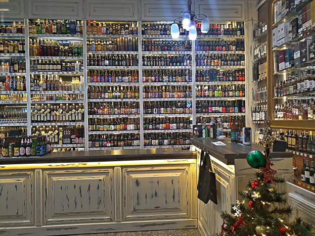 Ein Geschäft mit Regalen voller Spirituosenflaschen, einem geschmückten Weihnachtsbaum, einer Kommode mit Schubladen und von der Decke hängenden Lichtern.