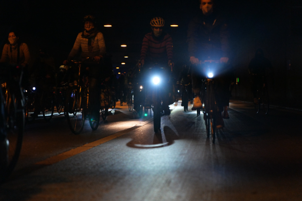 Eine Gruppe von Menschen, die nachts auf beleuchteter Straße mit Fahrrädern fahren, alle tragen Helme.