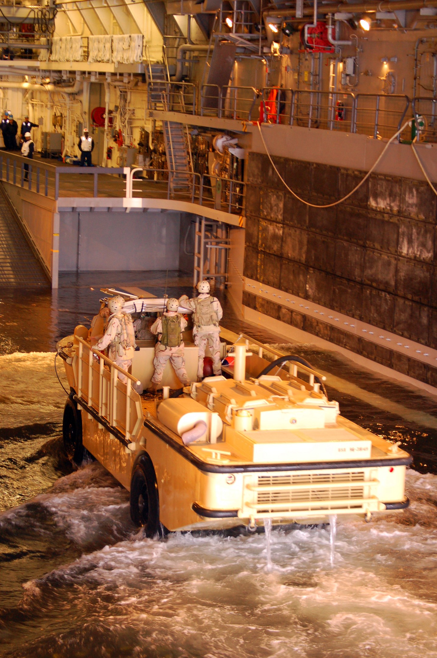 Amphibisches Fahrzeug mit Helmtr├Ągern durch Wasser in der N├Ąhe einer Wand, mit Menschen, Gel├Ąndern, Lichtern und Rohren im Hintergrund.