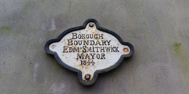 Plaque an der Seite eines Gebäudes, die die Borough-Grenze markiert, mit 'Edm Smithwick Mayor' in fetten weißen Buchstaben auf einem schwarzen Metallhintergrund.