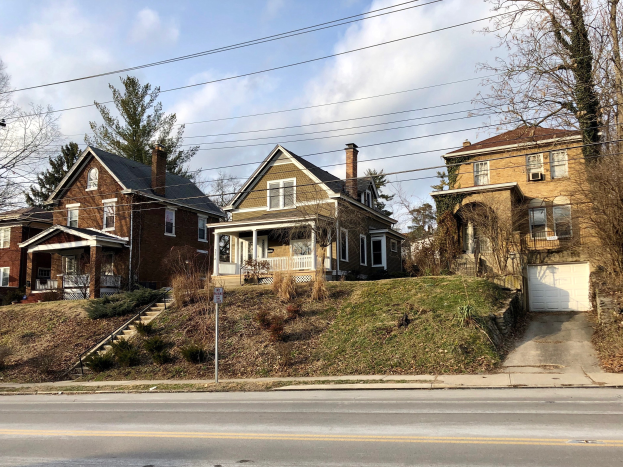 Reihe von Häusern mit Fenstern, Türen, Säulen, Geländern, Stufen, Pflanzen und einem Pfahl mit einer Tafel, die vor einem bewölkten Himmel steht und eines der teuersten Häuser zum Verkauf in Detroit, Michigan darstellt.