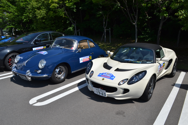 Zwei Porsche-Fahrzeuge nebeneinander in einer Parkanlage mit Bäumen im Hintergrund geparkt, jeweils mit Porsche Club Japan-Aufklebern versehen.