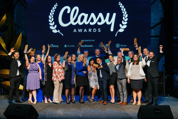 Gruppe von Menschen auf einer Bühne mit Auszeichnungen, Lautsprechern darunter und einem Bildschirm im Hintergrund mit "Classy Awards 2019"